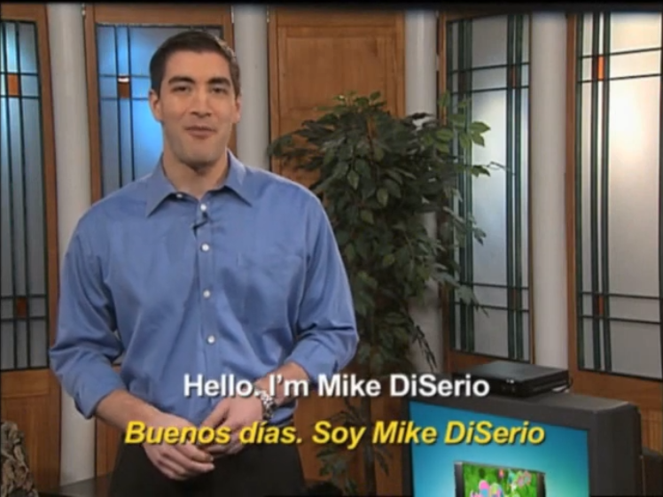 ID: Mike DiSerio from the National Association of Broadcasters introducing the nightlight program. He stands on the left with a blue button-down shirt and there's a television to his right. The captions read 'Hello. I'm Mike DiSerio', then repeat in Spanish at the bottom.